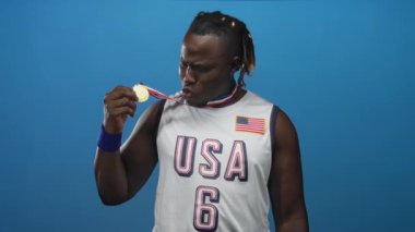 Bileklikleriyle parlak mavi bir stüdyoda gülümserken elinde bayraklı bir bayrakla altın madalya tutan ve pazılarını esneten bir adam. Zafer kutlamaları..