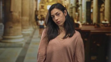 Kadın başını eğiyor, kilisenin iç kısımlarında kilise sıraları ve sütunlarıyla yüzünü gösteriyor; tefekkür ve inanç.