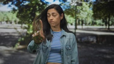 Kadın işaret parmağı, orman ortamında kot ceket ve çizgili hasat bluzu giyer, gözler küçümseyici bir hareketle kapanır..