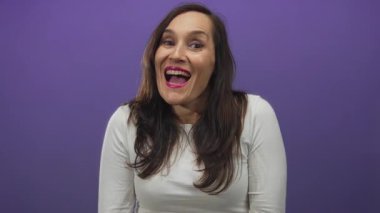 Canlı mor bir duvara gülümseyen İspanyol kadın beyaz gömlek giyiyor. Duygularla ve kişiliklerle dolu, izole edilmiş, canlı bir arkaplanı olan anlamlı bir anda yakalanmış.