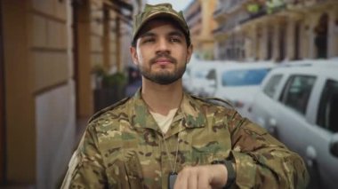 Kamuflaj üniformalı ve şapkalı adam şehirde araçlı metal künye zinciri gösteriyor..