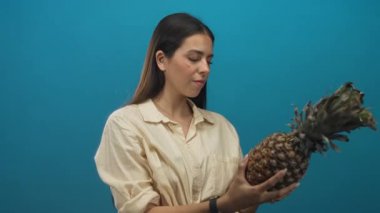 Stüdyoda ananas tutan ve çenesine dokunan genç esmer kadın, düşünceli doğal ürün..