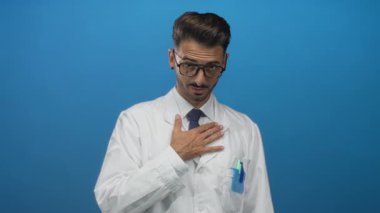 Mavi bir stüdyo duvarına dayanan beyaz önlüklü ve gözlüklü bir bilim adamı..