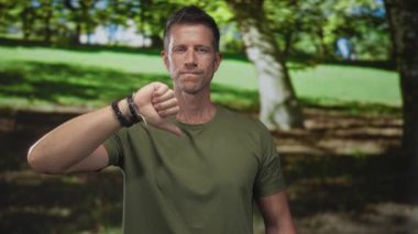Orman ortamında el ve önkoluyla baş parmak hareketi gösteren bir adam, eleştiri.