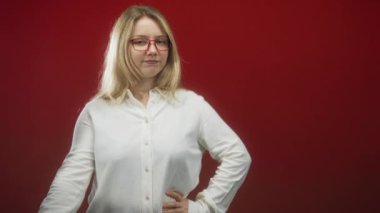 Sarışın, yüzünü sağ eliyle kapatan, sol eli kalçasında, kırmızı stüdyoda beyaz gömlek giyen, mahremiyet mahremiyeti mahremiyeti olan bir kadın..