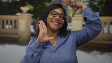 Sabahları gülümserken güneşli şehir caddesinde el ve gözlük takan kadın; yaratıcılık güveni.