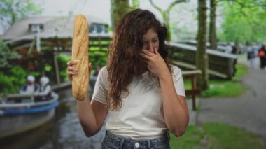 Beyaz tişört ve kot pantolon giyen kadın uzun baget tutuyor ve Amsterdam 'da burnunu sokakları kapatıyor; iğrenme kokusu reaksiyonu.