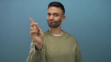Mavi arka planda el kol hareketi yapan genç bir adam, günlük süveter giyiyor, stüdyo ortamında ciddi duygular ifade ediyor benzersiz yüz ifadesini vurguluyor.