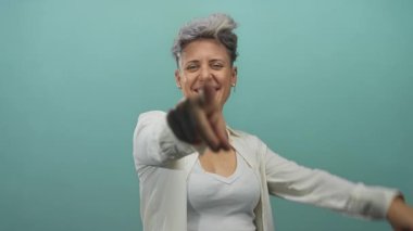 Bir stüdyoda yeşil bir arkaplanda parmaklarıyla gözünün yanında zafer jesti yapan kadın, kendine güveni kutluyor..