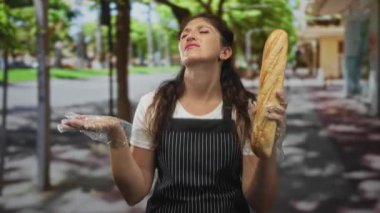 Eldivenli baget tutan, şehir kaldırımında çizgili bir önlükle omuz silken ve sokan bir kadın..