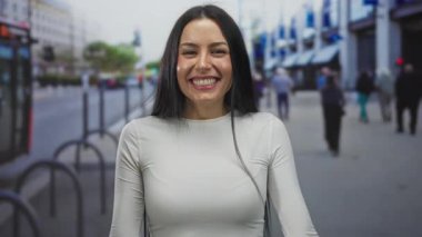 Şehir caddesinde neşeli bir ifadeyle gülümseyen kadın canlı şehir manzarası ve açık hava yaşam tarzının dinamik enerjisini sergiliyor.