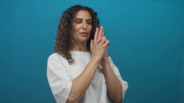 Genç İspanyol kadın mavi stüdyoda elleri kameraya dönük tabanca hareketi yapıyor..