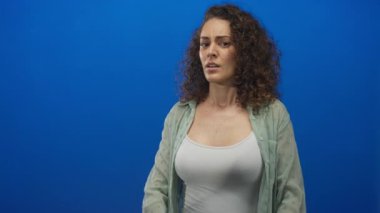 Avuç içleri açık genç İspanyol kadın mavi stüdyoda beyaz tank ve katıksız yeşil gömlek giyerek jesti durdurun..