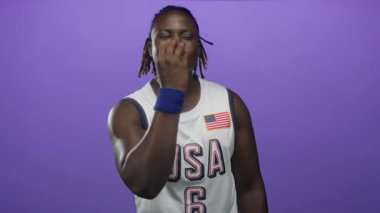 Amerika basketbol forması ve mavi bileklik giyen adam mor stüdyoda gülümsüyor..