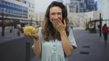 Kadın gülümsüyor ve elinde çıtır çıtır cipslerle sokakta el ele hareketler yapıyor. Mutluluk..