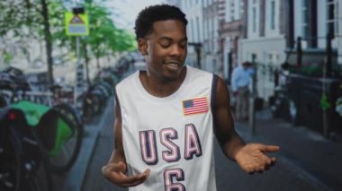 ABD Jersey 'deki adam, şehir caddesinde tuğla binalar ve park edilmiş bisikletlerle dolu açık avuç içleriyle el kol hareketleri yapıyor..