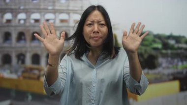 Kadın avuç içi kadar görünür bir şekilde elini kaldırır ve açık havada kolezyum binasının önünde gözlerini kapatır, yakınlarda bulanık kalabalık ve engeller; sakin yansıma.