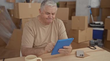 Paketlenmiş kutular ve kupalar arasında inşa ederken adamın elleri mavi tableti tıkırdatıyor; taşınma geçiş konsantrasyonu.