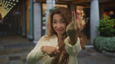 Orta parmağını gösteren ve diğer eliyle taş sütunlar ve vitrinlerle çerçevelenmiş bir şehir caddesini işaret eden kadın..