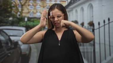 Gözlüklü kadın yumruğunu sıkıyor ve şehir caddesinde park halindeki arabaların ve demir çitlerin yanında avuç içine bastırıyor..