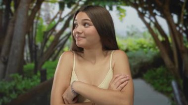 Genç kız, açık havada yemyeşil bir parkta çıplak omuzlarını silker ve şüpheci bir sırıtışla sırıtır; belirsizlik.