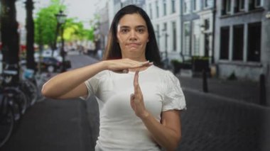 Gündelik beyaz bluzlu genç bir kadın güneşli bir şehir sokağında bisikletlerle dolu bir jest yapıyor. Kararlılık..