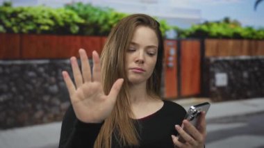 Gündüz vakti kaldırımdaki sokak girişinde akıllı telefona bakarken durması için elini kaldıran kadın..