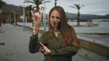 Latin kökenli genç bir kadın, elinde palmiyeli bir sokak gezinti güvertesinde taş boynuzları yapıyor; neşeli kaya tavrı..