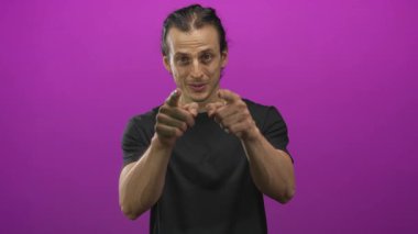 Mor bir stüdyoda iki eliyle kamerayı işaret eden adam, avuçlar ve parmaklar görünür ve çekici göz teması; eğlenceli bir davet.