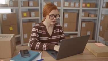 Dizüstü bilgisayarda yazan kadın, bir binada istiflenmiş nakliye kutularının arasında akıllı telefona uzanıyor; girişimciliğe odaklanıyor.