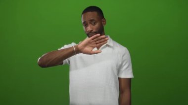 El sallayan bir adam, beyaz polo gömlek ve gümüş bilezik giyen, yeşil stüdyoda gülümseyen; dostça selamlaşma.