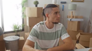 Evin anahtarlarını tutan ve gülümseyen bir adam, yığılmış karton kutular ve bir binanın içinde lamba arasında oturan, yeni ev gururu.