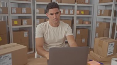 Dizüstü bilgisayarda yazan ve depolama binasındaki paketlerin arasındaki nakliye etiketlerini kontrol eden adam; küçük işletme verimliliği odaklı.