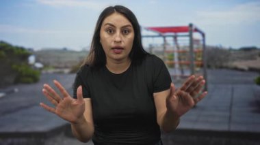 Kadın, oyun parkı parmaklıkları ve çatısı olan bir caddede dur işareti yapmak için iki elini de kaldırır..