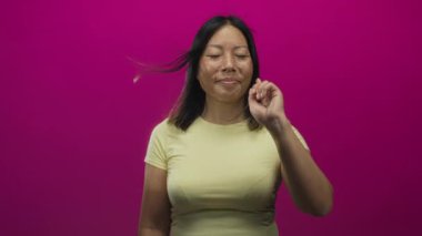 Genç İspanyol kadın, sarı t-shirt giyerken stüdyoda eflatun duvara karşı işaret ediyor; oyuncu özgüven.