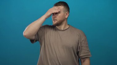 Eli alnında bir adam şakağı ovuyor mavi stüdyoda baş ağrısı, yorgunluk baş ağrısı.