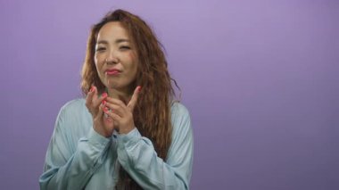 Eller birbirine kenetlenmiş ve avuçlar birbirine kenetlenmiş genç bir kadın, mor stüdyoda görünen kırmızı tırnaklar; şakacı bir umut..