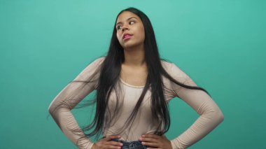 Kadın, parlak yumuşak ışıklandırma ve dalgalı saçlar altında canlı deniz mavisi stüdyosunda kalçalara dokunur..