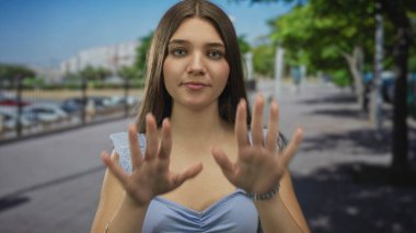 Mavi elbiseli genç beyaz kız avuçlarını boş güneş ışığı sokağında öne uzatıyor. Huzur ve esneklik..