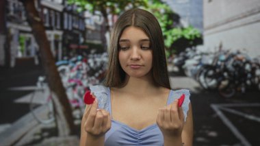 Alacakaranlıkta bir şehir caddesinde iki kırık kalp parçası taşıyan genç kız onlara bakıyor; kalp kırıklığı..