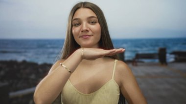 Kız gülümserken el ele tutuşuyor ve deniz kenarında güneşli bir sokakta kameraya bakıyor. Huzur..