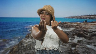 Genç İspanyol kadın uzanmış elleri ile işaret ve bir stüdyo plaj arkaplanı önce gülümseme; sıcak davet sevinç.