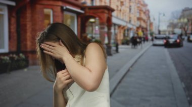 Tuğla dükkanlarıyla dolu kalabalık bir caddede elini yüzünü örten beyaz elbiseli kadın. Üzüntü kederi..