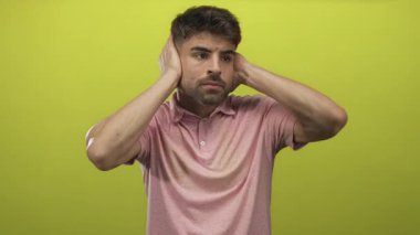 Genç ispanyol adam iki eliyle kulaklarını kapatır canlı yeşil stüdyo setinde rahatsızlık içinde somurturken; sıkıntı.