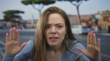 Genç kadın kulaklarını kapatıyor sonra da bulanık araba farları ve kentsel binalar arasında kalabalık caddede el sallıyor; heyecan.