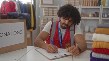Katlanmış giysi ve kutularla çevrili bağış merkezindeki panoda kalemle yazan adam, merhamet hizmeti.