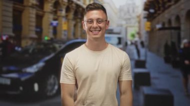 Gözlüklü, gülümseyen ve kalbi şekillendiren bir adam parmakları, elleri görünür, dar bir Avrupa caddesinde duruyor scooterları ve teslimat kamyoneti ile; sıcak dostça bir sevgi.