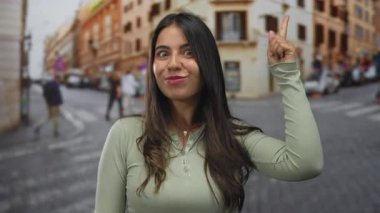 İşlek bir şehir sokağında gülümseyen bir ifadeyle işaret eden Latin kökenli genç bir kadın..