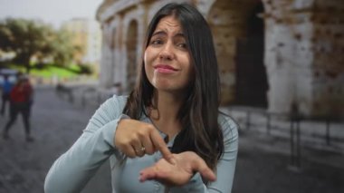 Genç İspanyol kadın, kadim bir binanın önünde el hareketini işaret ediyor; çaresizlik..