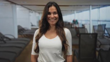 Gülümseyen ve ayakta duran bir kadın. Güvertede çıplak göğsü, şezlongları ve tavandan tavana pencereleri olan bir kadın..